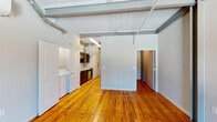 Located on Willow Street in Mount Airy, North Carolina, this single-floor unit showcases a distinctive industrial loft character achieved through the thoughtful renovation of what appears to be a historic commercial building. Original hardwood plank flooring runs throughout the entire space, complemented by exposed structural beams, painted wood-plank ceilings, and exposed conduit and ductwork that reinforce the building's industrial heritage. A prominent exposed brick accent wall anchors the main living area, which benefits from natural light through a large window overlooking the surrounding streetscape. A ceiling fan serves this open room. The kitchen is outfitted with dark espresso cabinetry, granite-style countertops, and a full suite of stainless steel appliances, including a refrigerator, electric range, over-the-range microwave, and dishwasher. An adjacent laundry area accommodates a full-sized washer and dryer. The bathroom features hardwood flooring continued from the main areas, a dark-cabineted vanity with a granite-top sink, and a tub-shower combination. A spacious walk-in closet with wire shelving provides generous storage. The overall ambiance balances historic character with modern, functional updates.