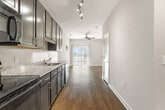 This thoughtfully laid-out one-bedroom, one-bathroom unit offers a functional and modern living experience across a single floor. The open-concept kitchen and living area forms the heart of the space, featuring rich dark-espresso cabinetry, granite countertops, black appliances including a range, microwave, dishwasher, and refrigerator, all complemented by wood-look plank flooring and track lighting overhead. The living area extends naturally from the kitchen, showcasing vaulted ceilings that lend a sense of openness well beyond the unit's footprint. A large sliding glass door floods the space with natural light and provides access to an outdoor view, while a ceiling fan adds comfort. The bedroom is a quiet, carpeted retreat with neutral tones and ample wall space. The bathroom is finished with matching dark cabinetry, a granite-top vanity, a large mirror, and the same wood-look flooring seen throughout the common areas. A dedicated closet and hallway complete the layout, offering practical storage and circulation. Clean lines, neutral walls, and consistent finishes throughout give the unit a cohesive, contemporary aesthetic suited for everyday living.