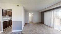This single-floor residential unit offers a well-organized layout designed for comfortable, everyday living. The living area is generously proportioned, featuring neutral-toned carpet, a textured ceiling, and a ceiling fan that contributes to a practical and airy atmosphere. Painted brick accent walls in both gray and white tones add a distinctive architectural character to the space, while vertical blinds along the sliding door allow for adjustable natural light and outdoor access.

The galley-style kitchen is efficiently arranged with rich dark wood cabinetry lining both sides, light speckled countertops, a stainless steel sink, and white appliances including a coil-top range and full-size refrigerator. Wood-look flooring runs throughout the kitchen, providing a clean, durable surface.

The bedroom is a comfortable retreat with plush carpeting, track lighting, and a wide sliding-door closet offering ample storage. An en-suite bathroom features tile-surround tub and shower combination, a toilet, and wood-look flooring. Additional storage is available via a hallway closet with sliding doors and open shelving, conveniently located near a vanity area. The unit is equipped with central HVAC venting throughout, ensuring year-round climate comfort.