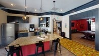 Located at 2510 Atlantic Palms Lane in North Charleston, SC, this single-floor community clubhouse is a thoughtfully designed gathering space that blends bold aesthetics with practical amenities. The interior is anchored by a striking open-concept kitchen featuring deep navy cabinetry, granite countertops, a crimson-accented island with bar seating, stainless steel appliances, and pendant globe lighting — offering a fully functional space for entertaining and everyday use.

The expansive lounge area is defined by a vivid floral-patterned carpet, eclectic furnishings including a leather sofa, built-in bench seating, and teal ottomans, all set against cream walls trimmed in bold navy crown molding. Dramatic red vertical wainscoting panels add a distinctive design element throughout. Large windows and wall-mounted flat-screen TVs enhance the social atmosphere.

A standout architectural feature is the full-width retractable glass garage door that opens the lounge directly to an outdoor poolside patio, allowing natural light to flood the interior and creating a seamless indoor-outdoor connection. Track and recessed lighting, along with mounted speakers, complete the clubhouse's well-appointed character, making it an ideal space for both casual relaxation and community events.