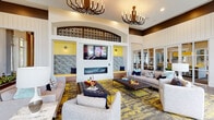 This single-floor clubroom in Jacksonville, FL (32258) is a thoughtfully designed community gathering space that blends contemporary style with inviting comfort. Soaring ceilings define the main lounge area, which is anchored by a sleek linear fireplace flanked by built-in accent niches finished in bold yellow. Above, an ornate laser-cut decorative screen frames an arched architectural detail, adding a striking focal point to the room. Two sculptural chandelier fixtures cast warm light over the seating area, which features neutral-toned sofas and chairs arranged atop vivid gold-and-charcoal patterned area rugs over large-format tile flooring.

Floor-to-ceiling windows along one wall flood the space with abundant natural light while offering views of palm trees and the surrounding grounds, with multi-panel glass French doors providing seamless connectivity between zones. Striped floor-length drapery in gold, gray, and white adds a refined, vertical accent throughout.

A dedicated bar and kitchen area includes warm wood cabinetry, white quartz countertops, a wall-mounted flat-screen TV, and green subway tile backsplash, complemented by pendant lighting and views to an outdoor terrace. A cozy banquette nook features velvet upholstery and a vibrant botanical mural, offering an intimate retreat within the larger communal space.