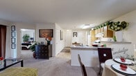 This single-floor residence offers a thoughtfully designed open-concept layout that seamlessly connects the kitchen, dining, and living areas. The kitchen is a functional centerpiece, featuring light maple cabinetry, granite-style countertops, a central island with a dark countertop, a double sink, a full suite of white appliances including a range with microwave above, and durable tile flooring. The open flow continues into the carpeted living room, which is defined by crown molding, soft neutral tones, and windows that bring in natural light.

The living area provides a comfortable and versatile space, while a separate den or flex room with carpet and a window offers additional functionality, ideal for a home office or study. The primary bedroom is carpeted and well-sized, complemented by a private en-suite bathroom featuring a walk-in glass-door shower, granite-style vanity, and tile flooring. A second bedroom is similarly carpeted and served by a full bathroom with a tub-shower combo and matching wood vanity with granite-style countertop. A dedicated in-unit laundry closet with a full-size washer and overhead shelving adds everyday convenience. The entry foyer provides a welcoming transition into the home's warm and cohesive interior.
