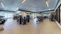 Located at 400 SW 27th Ave in Fort Lauderdale, Florida, this fitness center is a thoughtfully designed, single-floor facility built to support a comprehensive workout experience. The space features a clean, contemporary aesthetic with light wood-style flooring, crisp white walls accented by a bold dark horizontal stripe, and linear overhead lighting that keeps the environment bright and energizing.

The main workout floor is generously proportioned, housing a wide array of Life Fitness and Synrgy360 strength machines, free-weight benches, power racks with weight plates, and a dumbbell rack, catering to both strength training and functional fitness. Full-length mirrors line key sections of the walls, enhancing the sense of openness and allowing users to monitor their form.

A dedicated cardio zone features treadmills and elliptical machines positioned in front of large picture windows that frame views of lush tropical landscaping and a resort-style pool, bringing a refreshing outdoor connection to every workout. A separate glass-enclosed studio room provides a versatile space for group classes or focused individual training sessions.

Additional amenities include a water fountain station, a storage cabinet, and private rooms accessible from the main floor. Decorative wall art adds a refined touch to the overall atmosphere, making this fitness center both functional and visually inviting.