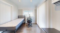 Located at 2335 Warring St in Berkeley, CA, unit 12A is a private bedroom offering a compact yet thoughtfully arranged living space. The room features warm hardwood flooring throughout, neutral-toned walls, and recessed lighting that contributes to a clean, well-lit environment. A large window fitted with horizontal blinds allows natural light to filter in while offering a view of the surrounding neighborhood, and vertical blinds provide an additional layer of privacy and light control. The bedroom is designed to accommodate both rest and productivity, with space for a twin bed and a dedicated study desk area complete with a task lamp. Built-in floor-to-ceiling cabinetry with a full-length mirror panel provides practical storage and enhances the sense of openness within the room. A wall-mounted mini-split air conditioning unit ensures personalized climate control year-round. A compact mini-fridge is conveniently situated near the entryway, adding a functional touch for everyday living. The private entry door, marked 12A, opens directly into this self-contained space, offering a degree of independence and privacy well-suited for a student or single occupant in the vibrant Berkeley community.