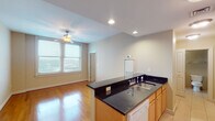 Located at 301 W Capitol St in Jackson, Mississippi, this single-floor unit offers a well-organized layout designed for comfortable living. The open-concept kitchen is outfitted with light maple cabinetry, dark granite countertops, a full suite of white appliances including a range, microwave, and refrigerator, and tile flooring that extends throughout the cooking area. The kitchen opens directly to the living space, which features gleaming hardwood floors and a pendant light fixture paired with a ceiling fan, creating a bright and welcoming atmosphere. Windows allow natural light to fill the main living area, offering views of the surrounding neighborhood. A central hallway connects the key spaces of the unit, finished with the same warm hardwood floors and flush-mount ceiling lighting. The bedrooms are carpeted for comfort, each equipped with a ceiling fan and closet storage, with windows providing additional natural light and outside views. The unit includes two bathrooms: one featuring a tiled tub-and-shower combination with a granite-topped vanity, and a second with a glass-enclosed walk-in shower, matching granite countertops, and tile flooring. Neutral, warm-toned walls throughout provide a cohesive and move-in-ready aesthetic across all rooms.