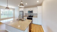 Located at 242 Bennington Hills Ct in West Henrietta, NY, this single-floor residence offers a thoughtfully designed layout with a clean, neutral aesthetic throughout. The kitchen serves as a central highlight, featuring crisp white cabinetry, granite countertops, stainless steel appliances including a refrigerator, electric range, and built-in microwave, and a large island with a double undermount sink illuminated by modern pendant lighting. Hardwood flooring runs through the kitchen and dining areas, transitioning to plush carpet in the living and bedroom spaces.

The living area is open and airy, connecting seamlessly to the kitchen via a half-wall partition. A front entry door and an arched accent window add architectural character to the space. Sliding glass doors lead to a private balcony with neighborhood views, bringing natural light into the interior.

Bedrooms are generously sized with large windows fitted with blinds, providing ample natural light. The walk-in closet is equipped with an extensive white wire shelving system, offering versatile storage configurations. The bathroom includes hardwood flooring, a tub-shower combination, a dark-finished vanity with granite countertops, and brushed nickel fixtures, completing the home's consistent, modern finishes.