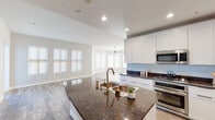 This well-appointed single-story home showcases a thoughtfully designed open-concept floor plan that seamlessly connects the kitchen, dining, and living areas. The kitchen serves as the centerpiece of the home, featuring rich dark granite countertops with striking veining, a large central island with a built-in sink, crisp white shaker-style cabinetry extending to the ceiling, a light blue tile backsplash, and a full suite of stainless steel appliances including a gas range, built-in microwave, dishwasher, and a side-by-side refrigerator with ice and water dispenser. Recessed lighting throughout the kitchen ensures a bright, functional workspace.

The adjacent living area is a standout architectural feature, boasting a gracefully curved wall of windows that floods the space with natural light. A ceiling fan anchors the room, which is finished with wood-look luxury vinyl plank flooring that flows consistently throughout the home, providing both durability and warmth.

The primary bathroom offers a clean, minimalist aesthetic with a wide white quartz vanity, a large frameless mirror, and a soaking tub with tile surround, complemented by a walk-in closet. The overall palette of soft neutral tones, white trim, and contemporary fixtures creates a bright, cohesive ambiance across the entire home.