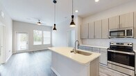 Located in Covington, Kentucky, this thoughtfully designed single-floor residence offers a clean, contemporary aesthetic throughout. The open-concept living and kitchen area serves as the heart of the home, featuring durable wood-look flooring, elevated ceilings, and abundant natural light streaming through multiple windows. A ceiling fan adds comfort to the spacious living area, which also provides access to the outdoors via a glass door.

The kitchen is a standout feature, equipped with light wood-toned cabinetry, a white subway tile backsplash, and a full suite of stainless steel appliances including a refrigerator, electric range, and microwave. A central island with a built-in sink and crisp white countertops provides both prep space and a casual gathering spot, accentuated by stylish pendant lighting overhead.

Two well-sized bedrooms feature plush carpeting and large windows that invite in natural light and outdoor views. Each room offers a calm, neutral palette suited to a variety of furnishing styles.

Two bathrooms serve the residence. One includes a sleek vanity with quartz-style countertops, a large mirror, and a tiled glass-enclosed shower. The second features a tiled soaking tub and shower combination alongside a matching vanity, with in-unit laundry conveniently located adjacent. The overall design is cohesive, modern, and move-in ready.