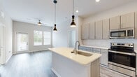 Located in Covington, Kentucky, this thoughtfully designed single-floor residence offers a clean, contemporary aesthetic throughout. The open-concept living and kitchen area serves as the heart of the home, featuring durable wood-look flooring, elevated ceilings, and abundant natural light streaming through multiple windows. A ceiling fan adds comfort to the spacious living area, which also provides access to the outdoors via a glass door.

The kitchen is a standout feature, equipped with light wood-toned cabinetry, a white subway tile backsplash, and a full suite of stainless steel appliances including a refrigerator, electric range, and microwave. A central island with a built-in sink and crisp white countertops provides both prep space and a casual gathering spot, accentuated by stylish pendant lighting overhead.

Two well-sized bedrooms feature plush carpeting and large windows that invite in natural light and outdoor views. Each room offers a calm, neutral palette suited to a variety of furnishing styles.

Two bathrooms serve the residence. One includes a sleek vanity with quartz-style countertops, a large mirror, and a tiled glass-enclosed shower. The second features a tiled soaking tub and shower combination alongside a matching vanity, with in-unit laundry conveniently located adjacent. The overall design is cohesive, modern, and move-in ready.