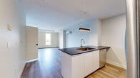 This thoughtfully designed bachelor unit at 6450 Bayers Road in Halifax offers a well-appointed, single-floor layout with modern finishes throughout. The open-concept kitchen and living area serves as the heart of the space, anchored by a sleek island featuring a dark countertop, an undermount sink with a pull-down faucet, and crisp white cabinetry. Stainless steel appliances — including a refrigerator, range, and microwave — complete the fully equipped kitchen, which is highlighted by contemporary pendant lighting. Light-toned hardwood-style flooring flows throughout, creating a warm and cohesive aesthetic. The living area benefits from a trio of large windows that invite an abundance of natural light and offer views of the surrounding neighbourhood. A wall-mounted mini-split unit provides efficient climate control. The bedroom area includes generous built-in closet storage, offering practical organization solutions. The bathroom is clean and modern, featuring a glass-enclosed walk-in shower with white tile surround. A dedicated laundry area houses a stacked front-load washer and dryer, adding everyday convenience. The overall ambiance is bright, contemporary, and efficiently designed, making excellent use of every square foot.