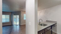 This single-floor residence offers a functional and well-organized layout designed for comfortable everyday living. The open-concept living and dining area features wood-look hard flooring and a subtle raised platform section, adding a distinctive architectural detail to the space. A ceiling fan with light fixture provides both comfort and illumination, while a sliding glass door floods the area with natural light and provides direct access to an outdoor patio with views of surrounding greenery.

The kitchen is defined by a wraparound peninsula counter with a stainless steel sink and modern gooseneck faucet, dark cabinetry, and a suite of black appliances including a refrigerator, range, and over-the-range microwave. A textured ceiling carries throughout the common areas, adding a classic residential character.

The bedrooms are carpeted and finished in neutral tones, each featuring window blinds that allow for natural light and privacy. The rooms offer generous wall space suitable for a variety of furniture arrangements.

Two bathrooms serve the residence. One full bathroom includes a tub-shower combination, a dark-cabinetry vanity with a white countertop sink, and wood-look tile flooring. A second bathroom features a similar vanity setup with a dedicated toilet area, providing added convenience for residents.