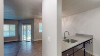 This single-floor residence offers a functional and well-organized layout designed for comfortable everyday living. The open-concept living and dining area features wood-look hard flooring and a subtle raised platform section, adding a distinctive architectural detail to the space. A ceiling fan with light fixture provides both comfort and illumination, while a sliding glass door floods the area with natural light and provides direct access to an outdoor patio with views of surrounding greenery.

The kitchen is defined by a wraparound peninsula counter with a stainless steel sink and modern gooseneck faucet, dark cabinetry, and a suite of black appliances including a refrigerator, range, and over-the-range microwave. A textured ceiling carries throughout the common areas, adding a classic residential character.

The bedrooms are carpeted and finished in neutral tones, each featuring window blinds that allow for natural light and privacy. The rooms offer generous wall space suitable for a variety of furniture arrangements.

Two bathrooms serve the residence. One full bathroom includes a tub-shower combination, a dark-cabinetry vanity with a white countertop sink, and wood-look tile flooring. A second bathroom features a similar vanity setup with a dedicated toilet area, providing added convenience for residents.