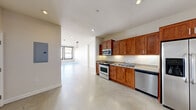This single-floor unit offers a thoughtfully designed layout that blends modern finishes with functional living spaces. The kitchen serves as a central highlight, featuring rich warm-toned wood cabinetry, granite countertops, and a full suite of stainless steel appliances including a range, microwave, dishwasher, and refrigerator with ice and water dispenser. Polished concrete floors extend throughout the open-plan living and kitchen areas, lending an industrial-chic aesthetic that is both durable and visually cohesive. Recessed lighting and pendant fixtures provide layered illumination throughout the space. The entry foyer is defined by a distinctive solid wood door with a transom window, flanked by interior doors offering closet and utility access. The living area transitions into a sun-filled space distinguished by large, black-framed windows with roll-down shades, offering expansive urban views and abundant natural light. A unique decorative mosaic tile border accents the floor near the windows, adding architectural character. Exposed ceiling beams further enhance the industrial aesthetic of the living zone. The bathroom is finished with classic white subway tile surrounding a full soaking tub and shower combination, complemented by a granite-topped vanity and tile flooring, creating a clean and timeless look.