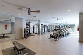 Located at 747 Ralph McGill Blvd NE in Atlanta, Georgia, this well-appointed fitness center offers a generously sized, single-level space designed to accommodate a comprehensive workout experience. The open floor plan is finished with light wood-style flooring throughout, contributing to a clean, modern aesthetic that makes the space feel bright and inviting.

The cardio zone is prominently featured, housing a long row of treadmills, elliptical machines, and stationary cycling bikes, all positioned to maximize use of the room's expansive layout. Multiple ceiling fans are mounted overhead, ensuring consistent airflow and comfort during workouts. Recessed lighting supplements the natural light that filters in through windows along one wall, keeping the space well-illuminated at all times.

The strength training area is equally well-equipped, featuring a multi-functional cable and power rack system suitable for a wide range of exercises. A dedicated dumbbell rack holds a full set of free weights, while adjustable benches provide flexible options for various lifting routines. Mirrored wall panels in select areas enhance the sense of space and allow users to monitor their form.

The facility maintains a clean, organized layout with rubber mats placed beneath equipment zones for safety and floor protection. Overall, the fitness center presents a professional, functional environment well-suited for both cardio and strength training routines.