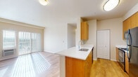 This single-floor residence offers a thoughtfully designed layout that balances functionality and comfort throughout its rooms. The open-concept kitchen flows seamlessly into the living area, creating a connected and airy feel. The kitchen is equipped with warm-toned wood cabinetry, white countertops, a peninsula with an undermount sink, and black stainless appliances including a refrigerator and range. Hardwood-style flooring runs throughout the kitchen and living areas, lending warmth and continuity to the space. The living area is bathed in natural light streaming through a sliding glass door fitted with vertical blinds, offering access to the outdoors. The bedrooms feature plush carpeting and are brightened by windows with horizontal blinds, providing views of the surrounding landscape. Baseboard heating units are present in the bedroom areas, ensuring year-round comfort. The primary bathroom features warm wood vanity cabinetry, a white countertop, a large mirror, and hardwood-style flooring. A second bathroom includes a full tub-shower combination with a curved curtain rod. Clean, neutral wall tones throughout the space create a bright and welcoming ambiance that is both versatile and move-in ready.