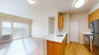 This single-floor residence offers a thoughtfully designed layout that balances functionality and comfort throughout its rooms. The open-concept kitchen flows seamlessly into the living area, creating a connected and airy feel. The kitchen is equipped with warm-toned wood cabinetry, white countertops, a peninsula with an undermount sink, and black stainless appliances including a refrigerator and range. Hardwood-style flooring runs throughout the kitchen and living areas, lending warmth and continuity to the space. The living area is bathed in natural light streaming through a sliding glass door fitted with vertical blinds, offering access to the outdoors. The bedrooms feature plush carpeting and are brightened by windows with horizontal blinds, providing views of the surrounding landscape. Baseboard heating units are present in the bedroom areas, ensuring year-round comfort. The primary bathroom features warm wood vanity cabinetry, a white countertop, a large mirror, and hardwood-style flooring. A second bathroom includes a full tub-shower combination with a curved curtain rod. Clean, neutral wall tones throughout the space create a bright and welcoming ambiance that is both versatile and move-in ready.