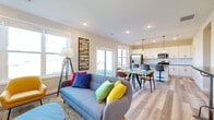 This two-floor home is designed with a contemporary aesthetic, combining functional layouts with modern finishes. The main level showcases an open-concept living, dining, and kitchen area unified by light-toned hardwood-style flooring. The kitchen is well-appointed with white shaker cabinetry, granite countertops, stainless steel appliances including a gas range and French door refrigerator, and pendant lighting. A sliding glass door in the dining area floods the space with natural light and provides outdoor access, while a round glass dining table anchors the area. The living room features a sleek fireplace with a tile surround and wood mantle, complemented by a staircase with modern metal railings leading to the upper floor. A convenient half bath and a dedicated laundry closet with full-size washer and dryer are also found on this level. Upstairs, the primary bedroom is spacious and well-lit with multiple windows, plush carpeting, and a ceiling fan. It is complemented by a generous walk-in closet with wire shelving. Neutral tones, recessed lighting, and black hardware accents contribute to a cohesive, modern feel throughout the home.