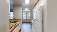 This single-story residence at 400 May Rd in Union City, California presents a well-organized layout with a clear separation between living, sleeping, and functional spaces. The galley-style kitchen is equipped with white cabinetry accented by wood trim, granite-look countertops, white appliances including a refrigerator, electric range, and dishwasher, and a skylight that fills the space with natural light. A window at the far end of the kitchen provides an outdoor view and adds to the overall brightness. The kitchen opens to the living area via a peninsula counter with a granite-look overhang, creating a convenient pass-through connection. The living room features neutral carpet, a large window with vertical blinds for natural light, and a tile-surround fireplace that serves as a focal point. Wood-style flooring transitions through the entry and kitchen areas. The bedroom is generously sized with plush carpet, a large window overlooking greenery, and direct access to a walk-in closet with built-in shelving. The bathroom includes a granite-look vanity, wood-style flooring, and a full tub-shower combination with clean white surround panels. The overall palette is neutral and light throughout.