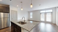 This single-floor residence showcases a thoughtfully designed open-concept layout that seamlessly connects the kitchen and living areas. The kitchen is a standout feature, anchored by a granite-topped island with an undermount sink and stylish pendant lighting overhead. Dark espresso cabinetry with sleek hardware lines the walls, complemented by a classic white subway tile backsplash and a full suite of stainless steel appliances, including a refrigerator, range, and built-in microwave. Rich, dark hardwood-style flooring flows throughout the main living areas, adding warmth and visual continuity to the space.

The bedrooms offer a comfortable retreat, finished with plush neutral carpeting and bright white walls. Each room is equipped with a ceiling fan and benefits from natural light streaming in through double windows fitted with blinds. The bathroom is clean and modern, featuring a soaking tub with a subway tile surround, brushed nickel fixtures, and wood-style flooring that ties back to the rest of the home.

Overall, the space presents a cohesive aesthetic defined by a contrast of dark cabinetry against light countertops and walls, creating a contemporary yet inviting atmosphere throughout.