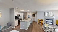 Located at Buckingham Station in Midlothian, VA, this one-bedroom, one-bathroom residence offers a thoughtfully designed single-floor layout that maximizes both comfort and functionality. The open-concept kitchen and living area serves as the heart of the home, where the kitchen impresses with white cabinetry, granite countertops, stainless steel appliances including a refrigerator and microwave, and a peninsula with an integrated sink — ideal for casual dining or entertaining. Hardwood-style flooring runs throughout the main living areas, adding warmth and continuity. The living room is a standout space, featuring a tile-surround fireplace with a white mantel, large sliding glass doors dressed with vertical blinds that invite natural light, and ample room for comfortable seating arrangements. The bedroom offers plush carpeting, a generous window overlooking lush greenery, and access to a dedicated closet, creating a calm and restful retreat. The bathroom is well-appointed with granite-topped vanity cabinetry, a full tub-shower combination with white tile surround, and wood-style flooring that ties the space together with a cohesive aesthetic. Neutral gray tones throughout provide a clean, modern backdrop suited to a variety of interior styles.