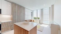 Located at 2100 N Central Rd in Fort Lee, NJ, this thoughtfully designed studio unit delivers a clean, modern aesthetic within a compact, efficiently laid-out single-floor plan. The open-concept living area is immediately striking, bathed in abundant natural light streaming through expansive floor-to-ceiling windows that frame lush treetop views. Light-toned hardwood flooring runs throughout, reinforcing the bright, airy atmosphere.

The kitchen is a standout feature, showcasing a sophisticated blend of high-gloss white upper cabinetry and warm wood-grain lower cabinets and panels. A sleek white quartz island with bar seating serves as both a functional workspace and a visual centerpiece. Stainless steel appliances and under-cabinet lighting complete the polished look.

A full-height wood-paneled wall with integrated storage and a Murphy bed provides smart, space-saving functionality in the living area, where a cozy seating nook nestles against the window wall to take full advantage of the outdoor views.

The bathroom is finished with marble-style wall tile, large-format floor tiles, a wood-fronted floating vanity with a white quartz countertop, and a glass-enclosed shower — all contributing to an upscale, spa-like feel. Overall, the space achieves an elegant balance of modern design and practical living.