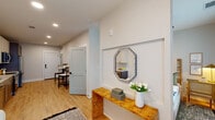 Located at 200 Henry Hill St in Cary, NC, this thoughtfully designed single-floor residence offers a cohesive blend of modern finishes and functional living spaces. The entryway sets an inviting tone with light hardwood-style flooring, recessed lighting, and a built-in niche accented by a decorative octagonal mirror and a warm burl wood console table. The kitchen is a standout feature, showcasing two-tone cabinetry — crisp white uppers paired with gray lowers adorned with gold hardware — complemented by a white subway tile backsplash, quartz countertops, and a full suite of stainless steel appliances. Open shelving adds character and practicality. The kitchen flows naturally into the living area, which benefits from natural light streaming through large windows. The bedroom is a serene retreat, featuring a ceiling fan, generous natural light from oversized windows with views of the surrounding community, and ample space for a desk or workspace. The bathroom features white shaker-style cabinetry, quartz countertops, and hardwood-style flooring that carries throughout the home. A dedicated in-unit laundry closet with a stacked washer and dryer adds everyday convenience. A dining nook with a marble-top table and an adjacent walk-in closet round out this well-appointed residence.