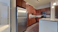 Located at 5800 Highlands Plaza Dr, this single-floor space offers a thoughtfully designed layout with modern finishes and functional details throughout. The kitchen is a standout feature, showcasing rich, warm-toned wood cabinetry that extends to the upper walls, providing ample storage. Stainless steel appliances — including a full-size refrigerator, built-in microwave, electric range, and dishwasher — lend a sleek, contemporary feel. The countertops feature a stone-look surface that complements the cabinetry, while a kitchen island offers additional workspace and convenience. Track lighting overhead ensures the area is well-lit, highlighting the clean lines of the design. The flooring throughout is a durable wood-look material in a warm, medium tone that ties the space together cohesively. The overall ambiance is modern yet inviting, with a neutral color palette that allows the warm wood tones of the cabinetry to serve as the focal point. The layout is practical and efficient, making it well-suited for everyday living. This single-floor design ensures easy accessibility and a seamless flow between the kitchen and the surrounding living areas.
