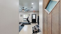 Located in Kissimmee, Florida, this dedicated fitness center offers a comprehensive and thoughtfully designed workout environment. The space features durable terrazzo-style flooring throughout, providing a clean, low-maintenance surface ideal for high-traffic exercise use. A large ceiling fan with integrated lighting keeps air circulating, while recessed lighting ensures the room is well-lit at all times.

The cardio zone is generously equipped with multiple treadmills, a stationary bike, and an elliptical trainer, all positioned to take advantage of the natural light streaming through several windows fitted with horizontal blinds. A full-length wall mirror spans one side of the room, visually expanding the space and allowing users to monitor their form during workouts.

The strength training area features an adjustable weight bench, a rack of dumbbells, a kettlebell, and a hanging Everlast punching bag, catering to a variety of fitness routines. A standout design feature is the wood slat accent wall, which anchors a wall-mounted flat-screen TV — ideal for entertainment during workouts. Adjacent to this wall is a private sauna room, adding a wellness and recovery dimension to the facility. The space is accessed through a solid black entry door and is equipped with an emergency exit sign, reflecting attention to safety standards.