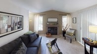 Located at 31500 1st Ave S in Federal Way, Washington, this single-floor residence offers a well-organized layout with distinct living, dining, sleeping, and kitchen areas. The living room is a standout space, featuring vaulted ceilings that lend a sense of openness and volume, a tiled fireplace as the focal point, and multiple windows that invite natural light and views of the surrounding greenery. Plush carpeting and neutral wall tones create a warm, comfortable atmosphere throughout the common areas. Adjacent to the living room, the dining area accommodates a full-sized dining set beneath a ceiling fan with integrated lighting and benefits from window access to natural light. The galley-style kitchen is efficiently designed, equipped with white appliances including a coil-top range, refrigerator, and dishwasher, complemented by warm wood cabinetry, light tile flooring, and ample counter space. The primary bedroom features a sliding-door closet, carpeted floors, and a bright window with curtains. A secondary bedroom provides additional flexibility, also carpeted and well-lit with a large window. The floor plan, as viewed from above, reveals a thoughtfully arranged multi-room layout with clear separation between living and sleeping zones, making this residence both functional and comfortable for everyday living.