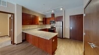Located at 1880 Old Hudson Road in Saint Paul, MN, this single-floor unit offers a thoughtfully designed layout with quality finishes throughout. The kitchen is a standout feature, showcasing rich cherry wood cabinetry, granite countertops, a large peninsula island, stainless steel appliances including a refrigerator, range, microwave, and dishwasher, and track lighting overhead — all set atop light hardwood-style flooring. The open living area flows directly from the kitchen, highlighted by large floor-to-ceiling windows and a glass door that flood the space with natural light and provide views of the surrounding neighborhood. The unit includes two bedrooms, both featuring plush carpeting and windows that allow for additional natural light. One bedroom includes a walk-in closet and direct access to a private bathroom. The bathrooms are finished with granite-topped vanities and rich wood cabinetry. One bathroom features a tub-shower combination with grab bars, while the other offers a shower and similar granite finishes. Additional storage is provided via a dedicated closet. The consistent use of warm tones, hardwood-style flooring in living areas, and neutral wall colors creates a cohesive and comfortable ambiance throughout the unit.