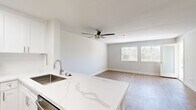 This thoughtfully designed single-floor residence offers a cohesive, modern aesthetic throughout its efficiently utilized layout. The open-concept kitchen and living area serves as the heart of the home, where a striking quartz waterfall-edge peninsula anchors the kitchen. White shaker cabinetry, stainless steel appliances — including a refrigerator, range, and microwave — and a stainless undermount sink complete the kitchen's clean, contemporary look. The living area flows seamlessly from the kitchen, featuring light wood-tone flooring, a ceiling fan, and a large window that frames views of lush greenery, including palm trees visible in the distance.

The spacious primary bedroom is finished with plush carpet, a ceiling fan with integrated lighting, and a window that fills the room with natural light. An exterior door in the bedroom opens to a private balcony overlooking verdant tree canopy, adding a tranquil outdoor connection. The full bathroom is outfitted with a tub-shower combination, a white vanity with a marbled countertop, and wood-look tile flooring, maintaining the home's clean and neutral palette.

Throughout the residence, neutral wall tones, consistent trim work, and an abundance of natural light create a bright, airy ambiance that feels welcoming and move-in ready.