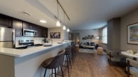 Located on Euclid Avenue in the heart of Cleveland, Ohio, this contemporary single-floor residence offers a thoughtfully designed open-concept layout that seamlessly connects the kitchen, dining, and living areas. The kitchen is a standout feature, outfitted with dark espresso cabinetry, stainless steel appliances, a white subway tile backsplash, and a generous peninsula with quartz countertops and bar seating — ideal for casual dining or entertaining. Track lighting and pendant fixtures illuminate the space with a modern aesthetic.

The living area is warm and inviting, anchored by rich hardwood-style flooring that runs throughout the main living spaces. Large windows allow natural light to fill the room, offering a bright and airy atmosphere. A dedicated sitting nook near the windows provides additional flexibility for relaxing or working.

The residence includes two well-sized bedrooms, each finished with plush carpeting and neutral tones that create a calm, restful environment. Both bedrooms have access to bathrooms featuring dark vanity cabinetry, quartz countertops, and tile flooring. The overall design palette — soft grays, warm browns, and crisp whites — lends a cohesive and contemporary feel throughout the entire space.