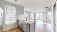 Located at 555 W 5th Ave in Columbus, Ohio, this one-bedroom, one-bathroom residence offers a well-designed open-concept layout. The kitchen is a standout feature, showcasing gray shaker-style cabinetry, granite countertops, a subway tile backsplash, stainless steel appliances including a range, over-the-range microwave, refrigerator, and dishwasher, and a peninsula with an undermount sink and pendant lighting above. Warm hardwood-style flooring extends throughout the main living areas, complementing the neutral gray walls and clean white trim.

The living room is bright and airy, featuring large windows and a glass door that invite abundant natural light and offer views of the surrounding Columbus cityscape. The bedroom is carpeted for comfort and includes generous windows that continue the home's connection to natural light. The bathroom features a wood-toned vanity with a granite countertop, undermount sink, matte black fixtures, and tile flooring, with a dedicated closet conveniently adjacent. A walk-in closet provides practical storage. The overall aesthetic is contemporary and cohesive, with a neutral palette and modern hardware details throughout.