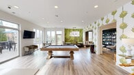 Located at 141 Wellington Pl in Cincinnati's vibrant Clifton neighborhood, this thoughtfully designed community amenity space offers a well-rounded environment for socializing and leisure. The single-floor layout is unified by light wood-look flooring throughout, white ceilings with recessed lighting, and bold botanical-print wallpaper featuring an artichoke motif that lends a distinctive, contemporary character to the space.

The main gathering area is anchored by a substantial wood-framed billiard table and opens into a dining lounge highlighted by a dramatic green accent wall, a striking globe chandelier, and built-in banquette seating paired with marble-top tables. A dedicated lounge alcove offers a more intimate retreat, furnished with mid-century-inspired seating, a stone-clad accent wall with a mounted flat-screen TV, and curated shelving.

The kitchenette is well-appointed with dark cabinetry, gold hardware, a white quartz countertop, a stainless steel refrigerator, and a herringbone tile backsplash, alongside a central island with bar stool seating. Large glass sliding doors connect seamlessly to an outdoor patio furnished with lounge seating — bringing in abundant natural light and extending the social space outdoors.
