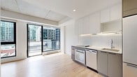 Located at 250 Rue Young in Montréal's vibrant Griffin town neighbourhood, this thoughtfully designed studio unit makes efficient use of its single-floor layout. The open-concept living and kitchen area is anchored by light oak hardwood flooring that runs throughout, creating a warm and cohesive aesthetic. Exposed concrete ceiling details add an industrial character, while a wall of floor-to-ceiling windows floods the space with natural light and offers urban cityscape views, with access to a private balcony.

The modern kitchen is well-appointed with two-tone cabinetry — white upper cabinets complemented by grey lower units — and a white subway tile backsplash. Full-sized stainless steel appliances include a built-in oven, induction cooktop, integrated dishwasher, and a full-height refrigerator-freezer, maximizing functionality within a compact footprint. A split-system air conditioning unit ensures year-round comfort.

A discreet built-in closet conceals a stacked washer and dryer unit, providing the convenience of in-unit laundry. The bathroom is clean and contemporary, featuring floor-to-ceiling white tile, a glass-enclosed walk-in shower, a wall-mounted medicine cabinet mirror, and a wood-accented vanity. Every element of this unit is designed for efficient, modern urban living.