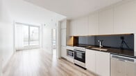 Located at 2061 Rue Stanley in the heart of downtown Montréal, this thoughtfully designed one-bedroom, one-bathroom unit offers a clean, modern aesthetic throughout. Light hardwood flooring runs continuously across the open-plan layout, contributing to a bright and cohesive feel.

The kitchen is a standout feature, outfitted with floor-to-ceiling white cabinetry, a dark granite countertop, a sleek dark tile backsplash, and stainless steel appliances including a full range with oven and built-in microwave. The open connection between the kitchen and living area maximizes the sense of space and encourages a functional flow.

The living area is bathed in natural light thanks to large floor-to-ceiling windows that frame views of the Montréal cityscape, creating an airy and inviting atmosphere. The bedroom continues this theme with its own generous windows and city-facing outlook, complemented by grey curtains for privacy and light control.

The bathroom is finished in neutral toned tiles with a wall-mounted toilet, a floating vanity topped with a dark granite counter, an under-mounted basin, and a mirrored medicine cabinet with integrated lighting — delivering a clean, contemporary spa-like feel.

A dedicated closet provides practical storage, completing this efficiently planned and stylishly finished urban residence in one of Montréal's most vibrant neighborhoods.