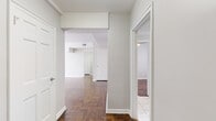 This single-floor unit showcases a cohesive, light-filled interior defined by rich parquet hardwood flooring laid throughout the main living areas and bedrooms. Neutral gray-white walls provide a clean, versatile backdrop across all rooms, lending a bright and open atmosphere.

The entry hallway connects the living spaces efficiently, with architectural soffits adding subtle definition between zones. The spacious living area features continued parquet flooring, multiple ceiling vents, and access to additional rooms via classic six-panel white doors with ample closet storage.

The kitchen is outfitted with white cabinetry, granite-style countertops, and stainless steel appliances including an electric range, built-in microwave, and dishwasher. Marble-look tile flooring and a large window overlooking greenery complete this functional space.

The bedrooms receive generous natural light through large multi-pane windows dressed with sheer white curtains, with parquet flooring and radiator heating units present in each room.

The bathroom features classic white wall tile, a soaking tub, pedestal-style vanity, and mosaic tile flooring, with a bright window providing natural ventilation and light. Overall, the unit presents a well-maintained, classic interior with consistent finishes throughout.