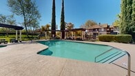 This residential complex, situated at 300 Peppertree Way in Pittsburg, California, showcases a Mediterranean-inspired architectural design. The property's centerpiece is a large, inviting swimming pool surrounded by a spacious concrete deck, perfect for sunbathing and relaxation. Adjacent to the pool, a covered pergola area provides shade and seating, creating an ideal spot for outdoor gatherings.

The landscaping is meticulously maintained, with mature cypress trees adding vertical interest and privacy to the grounds. Well-manicured hedges and lawns contribute to the overall aesthetic appeal. The complex features multi-story residential buildings with a neutral color palette, balconies, and large windows that likely offer ample natural light to the interiors.

Communal areas are thoughtfully designed, including a covered patio space with tables and chairs for resident use. The property is secured with wrought iron fencing, enhancing safety while maintaining an open feel. Concrete walkways connect various areas of the complex, ensuring easy navigation for residents.

Additional amenities appear to include storage facilities and possibly a clubhouse or community center. The overall ambiance of the complex suggests a resort-like atmosphere, providing residents with a comfortable and attractive living environment that balances private and shared spaces.