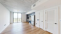 Located at 307 SW 5th St in Fort Lauderdale, FL, this contemporary single-floor unit offers a thoughtfully designed open layout with clean, modern finishes throughout. The living area is anchored by light-toned hardwood floors and exposed concrete ceilings that lend an industrial-chic character to the space. Floor-to-ceiling sliding glass doors open onto a private balcony, framing sweeping panoramic views of the Fort Lauderdale skyline and lush surrounding greenery, filling the interior with abundant natural light. The integrated kitchen is outfitted with slate-gray cabinetry, stainless steel appliances including a refrigerator, range, and microwave, making it both functional and visually cohesive with the overall aesthetic. A dedicated closet provides convenient storage directly off the main living area. The bathroom is a standout feature, showcasing large-format stone-look wall tiles, a frameless glass-enclosed walk-in shower with mosaic tile flooring, an LED-backlit vanity mirror, and crisp white fixtures that complete the upscale feel. The unit's open-concept design, refined material palette, and elevated outdoor views combine to create a polished and inviting living environment in the heart of Fort Lauderdale.