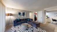 Located at 6006 E 126th St in Grandview, Missouri, this single-story unit offers a thoughtfully arranged floor plan designed for comfortable everyday living. The living room serves as the heart of the space, featuring plush carpeting, a textured ceiling, and a large sliding glass door that floods the room with natural light while providing direct access to an outdoor area with pleasant exterior views.

The kitchen is finished with rich, dark-stained cabinetry, dark granite-style countertops, tile-look flooring, and black appliances including a full-size refrigerator and range. Adjacent to the kitchen, a dedicated dining area accommodates a round table and seating for several guests, enhanced by a pendant light overhead and a pass-through counter connecting to the kitchen.

The bedrooms are carpeted and well-proportioned, each featuring closets with panel doors. The primary bedroom includes a ceiling fan, a window with natural light, and ample room for a full furniture arrangement. Additional bedrooms offer closet storage and neutral wall tones. The bathroom features a warm wood-toned vanity, white countertop, and a framed mirror. Throughout the unit, a consistent neutral gray palette and carpet flooring create a cohesive and welcoming ambiance.