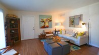 Located at 3857 Flowerfield Rd in Norfolk, Virginia, this single-floor home offers a well-organized layout designed for comfortable living. The open-concept living and dining area is anchored by warm hardwood-style flooring that flows seamlessly throughout the main living spaces. Vertical blinds along a large window-lined wall allow for flexible light control, while a stylish globe pendant light illuminates the dining area. A coat closet near the entry provides convenient storage just inside the front door.

The galley-style kitchen features warm wood cabinetry, a double-basin sink, countertop workspace on both sides, and white appliances including a refrigerator, stove, and dishwasher — all arranged for efficient use of space.

The home includes multiple bedrooms, each carpeted for comfort. The primary bedroom is generously sized with a tray ceiling detail, a large window for natural light, and built-in closet space. A second bedroom offers a classic wood spindle bed frame aesthetic and wall-mounted art, adding character to the space. Both bedrooms feature ample closet storage.

The bathroom is cleanly appointed with a full tub-shower combination, wood-toned flooring, a vanity with countertop storage, and a rustic wood floating shelf for additional organization. Throughout the home, neutral wall tones create a bright, cohesive ambiance.