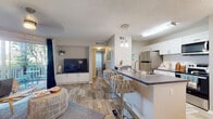 Located at 5412 Deerbrooke Creek Cir in Tampa, FL, this single-floor residence offers a thoughtfully designed open-concept layout that seamlessly connects the living, dining, and kitchen areas. Light wood-look flooring runs throughout, contributing to a bright and cohesive aesthetic.

The kitchen is a functional centerpiece, featuring white cabinetry, a full suite of stainless steel appliances, a subway tile backsplash, and a peninsula with a dark countertop and seating for bar-height stools — ideal for casual dining or entertaining. Pendant lighting above the peninsula adds a modern touch.

The living area is open and welcoming, with neutral walls, a textured ceiling, and ample natural light from multiple windows dressed with sheer curtains. A dedicated dining space accommodates a round wooden table and chairs, accented by coastal-inspired wall décor and a large window that brings in natural light.

The bedrooms are generously proportioned, each featuring large windows with sheer drapery, wood-look flooring, and ceiling fans. One bedroom includes a built-in desk nook, offering a quiet workspace bathed in natural light.

The bathroom is clean and well-finished, with white cabinetry, a dark countertop vanity, a full soaking tub with tiled surround, and floating wooden shelves for added storage. The overall ambiance of the home is relaxed and coastal, with warm tones and carefully considered details throughout.