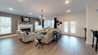 Located at 1601 Riddick Ln in Savannah, Georgia, this single-floor community space combines comfort and style in a thoughtfully designed open-concept layout. The main lounge area is anchored by a sleek electric fireplace set against a charcoal accent wall, complemented by recessed lighting and an elegant chandelier overhead. Large windows dressed with navy curtain panels flood the space with natural light and offer views of the surrounding community, while French doors provide direct access to the outdoor area. Rich hardwood-style flooring flows throughout, tying the space together seamlessly. The lounge is furnished with a generous sectional sofa, accent chairs, and coordinated décor, creating a welcoming and versatile gathering environment. A bar-height dining table with stools provides an additional seating option near the French doors. The kitchen is outfitted with deep espresso cabinetry extending to the ceiling, light quartz countertops, a stainless steel double-basin sink, subway tile backsplash in a soft blue-gray hue, and stainless steel appliances. A wide breakfast bar offers additional counter space and informal seating. Together, these elements create a polished, functional, and inviting community environment suited for socializing and everyday use.