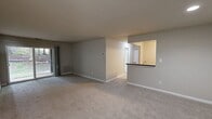 This single-floor, 1-bedroom, 1-bathroom residence offers 2,930 square feet of living space with a functional, well-organized layout. The unit is accessed through a dedicated entrance and flows into a combined kitchen and living room area. The kitchen is equipped with white cabinetry, dark countertops, and includes appliances such as a refrigerator, electric range, and over-the-range microwave, all set over durable wood-look flooring. The spacious living room features neutral-toned carpet, soft beige walls, and a sliding glass door that opens to views of a lush, wooded outdoor area with mature trees — providing a peaceful, natural backdrop. The 160-square-foot bedroom is carpeted with a large window offering additional garden views, and includes a closet with bi-fold doors along with direct access to the bathroom. The bathroom is clean and straightforward, featuring a full tub-shower combo with white subway tile surround. A generously sized additional carpeted room with recessed lighting, white bi-fold closet doors, and neutral walls provides flexible space for various uses. The property's exterior is surrounded by greenery, mature trees, and a natural stream, enhancing the overall tranquil ambiance of this residence.