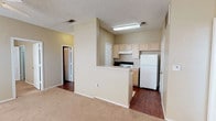 Located at 5917 67th St in Lubbock, TX, this single-story unit offers a practical and comfortable layout designed for everyday living. The open-concept floor plan connects the living area and kitchen seamlessly, creating a functional shared space. The living area features neutral-toned carpet, while the kitchen transitions to durable hardwood-style flooring. A half-wall peninsula divides the two spaces and provides additional counter space, making it ideal for casual dining or meal prep. The kitchen is equipped with light wood cabinetry, a white electric range, a full-size refrigerator, and an under-cabinet range hood. Ample upper cabinet storage keeps the kitchen organized and efficient. The textured ceiling and flush-mount and fluorescent lighting fixtures provide consistent illumination throughout. The bathroom features a single-sink vanity with light wood cabinetry, a large mirror with overhead lighting, additional overhead cabinetry for storage, and tiled walls near the shower area. A generously sized walk-in closet with dual wire shelving and hanging rods offers substantial storage for clothing and accessories. The overall color palette throughout the unit is warm and neutral, contributing to a clean and understated ambiance.