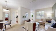 This single-story residence offers a well-organized layout with a series of functional and comfortable living spaces. The open living room serves as the centerpiece of the unit, featuring plush carpeting, a textured ceiling, and large windows that invite generous natural light and views of surrounding greenery. A bold sage green accent wall adds a distinctive design element to the space, complementing the otherwise neutral color palette throughout.

The galley-style kitchen is efficiently arranged with white cabinetry, dark countertops, hardwood-style flooring, and white appliances, including a range and refrigerator. It connects seamlessly to the main living and dining areas.

Two carpeted bedrooms provide comfortable retreats, each equipped with windows that offer outdoor views and ample wall space. The primary bedroom benefits from access to an en-suite bathroom, while a second full bathroom serves the remaining bedroom and guests. Both bathrooms feature white vanity cabinetry, single-sink countertops, and tub-shower combinations with tile flooring.

A dedicated laundry area houses a full-sized side-by-side washer and dryer with overhead shelving, adding practical convenience. Overall, the residence presents a clean, bright, and livable environment with a cohesive neutral aesthetic throughout.