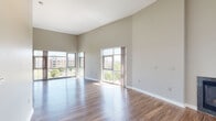 Located in Denver's vibrant Stapleton neighborhood, this single-floor residence at 7488 E 29th Ave offers a thoughtfully designed open-concept layout with striking architectural details throughout. Soaring vaulted ceilings create an expansive sense of volume across the main living and dining areas, which are bathed in natural light from oversized floor-to-ceiling windows overlooking the surrounding urban landscape and mature trees.

Rich hardwood flooring flows through the main living spaces, anchoring the open floor plan and connecting the living area to the kitchen. The kitchen is outfitted with white cabinetry, stainless steel appliances including a refrigerator, range, and microwave, and features a curved peninsula with dark granite countertops — an elegant focal point that also provides additional seating and prep space. Track lighting highlights the kitchen's high ceilings and modern finishes.

The bedroom is generously sized with plush carpeting, soaring ceilings, multiple windows offering neighborhood views, and a spacious walk-in closet. An en-suite bathroom with granite countertops and wood-look flooring adds convenience and continuity of design. In-unit laundry is also included, with a full-size washer and dryer tucked neatly into a dedicated space. The overall ambiance is bright, clean, and contemporary.