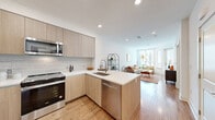 This thoughtfully designed one-bedroom, one-bathroom unit in the 94597 zip code offers a modern aesthetic throughout its efficiently organized single-floor layout. The open-concept kitchen and living area serves as the heart of the home, where light wood-grain cabinetry, a marble-style tile backsplash, and stainless steel appliances—including a range, over-the-range microwave, dishwasher, and French door refrigerator—create a sleek, contemporary kitchen. A peninsula island with a built-in sink and seating provides additional workspace and casual dining. Recessed lighting and warm hardwood-style flooring carry throughout the main living space, which is brightened by large windows that draw in abundant natural light. The living area offers a comfortable, airy atmosphere with views to the outside through a glazed door. The bedroom is a quiet retreat with a window, neutral white walls, and direct access to the walk-in closet, which features adjustable shelving and hanging rods. The bathroom is finished with large-format marble-look tile flooring, a floating wood vanity with a white countertop, a wide mirror, and a full soaking tub with shower. In-unit laundry is also included, adding everyday convenience.
