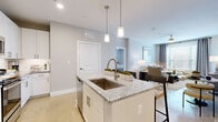 This 2-bedroom, 3-bathroom single-floor residence offers a cohesive, modern design highlighted by light-toned polished concrete floors, soft neutral walls, and abundant natural light throughout. The open-concept kitchen features a central island with granite countertops, an undermount sink, and pendant lighting overhead, flowing seamlessly into the living area. White shaker-style cabinetry, stainless steel appliances, and a tiled backsplash complete the kitchen's clean, contemporary aesthetic. The living room is bright and welcoming, with large windows dressed in elegant curtain panels and a ceiling fan for added comfort. The primary bedroom is a well-sized retreat with a ceiling fan, large window, and direct access to a dedicated bathroom featuring a granite-topped vanity and a walk-in closet with built-in shelving. The second bedroom mirrors the same calm, neutral palette with natural light and a ceiling fan. Each of the three bathrooms is finished with granite countertops, white cabinetry, and tub-shower combinations. Two closets provide ample storage, and a connecting hallway ties the layout together efficiently. The overall ambiance is clean, modern, and inviting.
