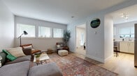 This well-maintained single-floor unit offers a comfortable and functional layout ideal for everyday living. The living room serves as the heart of the space, featuring light gray walls, smooth ceilings, and light-toned hardwood-style flooring that runs throughout the main areas. A row of windows fitted with white blinds allows generous natural light to fill the room, creating a bright and airy atmosphere. The space accommodates a sectional sofa, accent chairs, and a coffee table with ease, lending a relaxed yet organized feel.

The kitchen is efficiently designed with white shaker-style cabinetry, clean white countertops, and stainless steel appliances including a dishwasher and range. A window above the sink provides additional natural light, enhancing the crisp, tidy aesthetic of the space.

Two bedrooms offer cozy retreats, each carpeted and featuring windows with white blinds that invite natural light. Both rooms provide ample space for a bed and furnishings, with clean white walls offering a neutral backdrop.

The bathroom is well-appointed with light wood-look flooring, a full soaking tub with white subway tile surround, a separate glass-door shower, and a vanity with storage. Clean white walls and simple décor complete the fresh, functional design throughout this inviting unit.